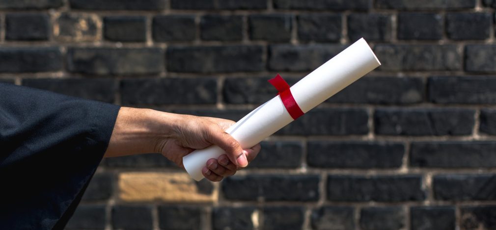 student-holding-out-diploma-by-wall